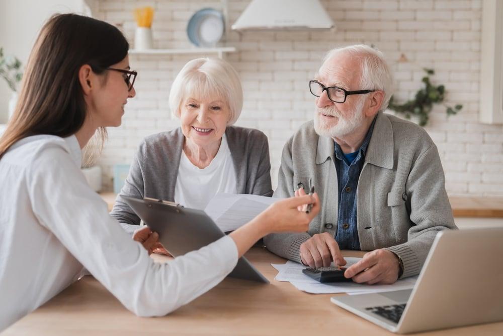 Life settlement policy review - show retired couple with agent in discussion at the table with computer depicting illustration review